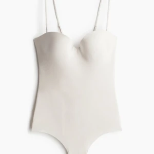 Body HM - blekbeige - En blekbeige/vit body från HM i mikrofiber med reglerbara, avtagbara axelband och vaderade kupor med bygel. Knäppning med hyskor och hakar. Fodrad gren med dolda tryckknappar. Helt ny och oanvänd med prislapp kvar! Helt slutsåld på HM! 