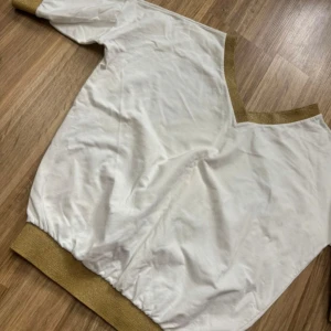 Vit tröja med guld detalj - Nyköpt begagnat tröja som tyvärr inte passade min smak. Provar då och säljer till någon annan som har nytta av tröjan. Tröjan är vit med guldkant längst med. 3/4 ärmar. Storlek M och är normal i storleken. Normal längd likaså.