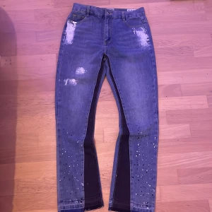 Blå jeans med slitningar och pärlor från Gallery Dept (pris kan diskuteras). - Unika blå jeans från Gallery Dept. med coola slitningar och pärldetaljer. De har en klassisk femficksdesign och en bekväm passform. Perfekta för dig som vill sticka ut med en edgy stil.