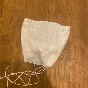 Vit glittrig diadem - Snyggt vitt diadem med glittrig yta. Perfekt för att ge en extra touch till din outfit. Diademet har en enkel design med band som knyts under hakan.