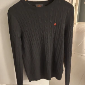 Grå stickad tröja från Morris - Säljer en stilren grå stickad tröja från Morris i 100% merinoull. Tröjan har ett diskret mönster och en liten broderad logga på bröstet. Perfekt för kyliga dagar.