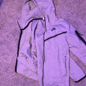 Grå hoodie från Nike - Säljer en grå hoodie från Nike med dragkedja .Den har en klassisk design med Nike-logga på bröstet och är perfekt för en avslappnad stil.