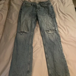 Blå jeans med hål vid knäna - Snygga blå jeans med slitningar på knäna. De har en klassisk femficksdesign och en bekväm passform. Perfekta för en avslappnad stil.