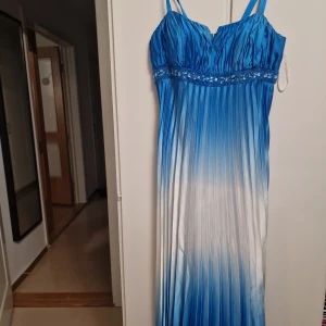 Blå och vit långklänning - Elegant långklänning med ombre-effekt i blått och vitt. Klänningen har smala axelband och vackra detaljer med paljetter under bysten. Perfekt för en speciell kväll.