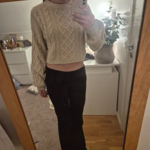 Beige stickad tröja - Säljer en mysig beige stickad tröja med flätmönster. Tröjan är croppad och har långa ärmar med ribbade muddar. Perfekt för kyliga dagar!