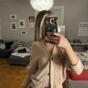 Beige stickad kofta från lager 157 - Mysig beige stickad kofta från lager 157 med knappar framtill. Perfekt för kyliga dagar med sin avslappnade passform och långa ärmar. En stilren och bekväm tröja att ha i garderoben.