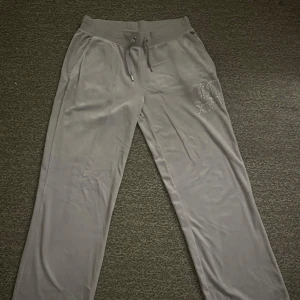 Grå mjukisbyxor från Juicy Couture - Snygga grå mjukisbyxor från Juicy Couture med glittrande stenar som bildar texten 'Juicy' på baksidan. 