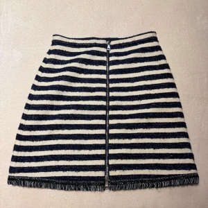 Randig kjol med dragkedja från Sonia Rykiel - Snygg kortkjol med marinblå och vita ränder. Kjolen har en framträdande dragkedja och fransdetaljer vid fållen. Perfekt för en stilren look.