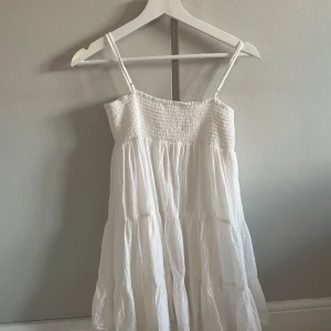 Vit klänning från Zara - Söt vit klänning från Zara med smala axelband och smockdetaljer upptill. Perfekt för varma sommardagar med sin luftiga design och korta längd. Endast använd ett få tal gånger, så inte tecken på användning!💗