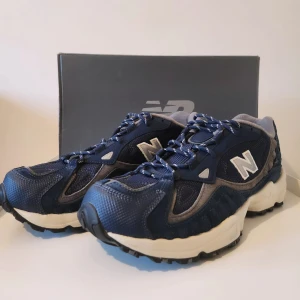 New Balance sneakers i blått och vitt - Snygga New Balance sneakers i blått med vita detaljer. Skorna har en robust sula och snörning för optimal passform. Perfekta för både stad och terräng.