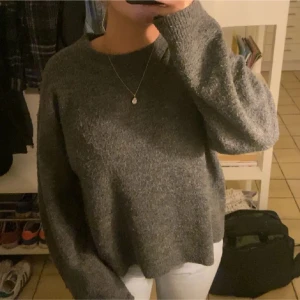 Grå stickad tröja - Mysig grå stickad tröja med långärmad design. Perfekt för kyligare dagar och ger en avslappnad look. Passar bra till jeans eller kjol.