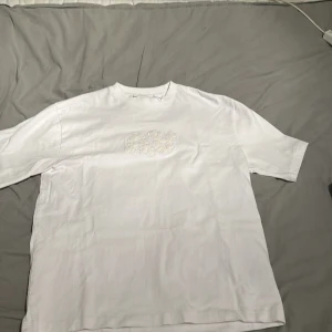 Vit t-shirt från Axel Arigato - En Oanvänd Axel Arigato T shirt med ovanligt tryck som är köpt på NK i Göteborg men aldrig använts då de var ett spontanköp som sedan ledde till att den bara blivit liggandes. Köptes för 1499kr. Storlek S men sitter oversized.