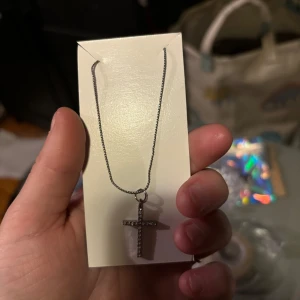 Silverfärgat halsband med korshänge - Elegant silverfärgat halsband med ett korshänge dekorerat med små stenar. Perfekt för att ge en stilren touch till din outfit.