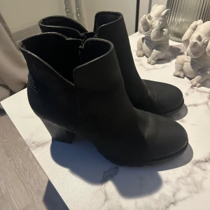 Svarta boots med klack - Snygga svarta boots från Clarks med klack och dragkedja på sidan. Perfekta för både vardag och lite finare tillfällen. Tillverkade i ett stilrent material som ger en elegant look.
