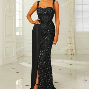 Svart glittrig långklänning från Missord - Elegant svart långklänning med glittrande paljetter och en smickrande slits. Klänningen har breda axelband och en figurnära passform som framhäver silhuetten. Perfekt för en glamorös kväll.