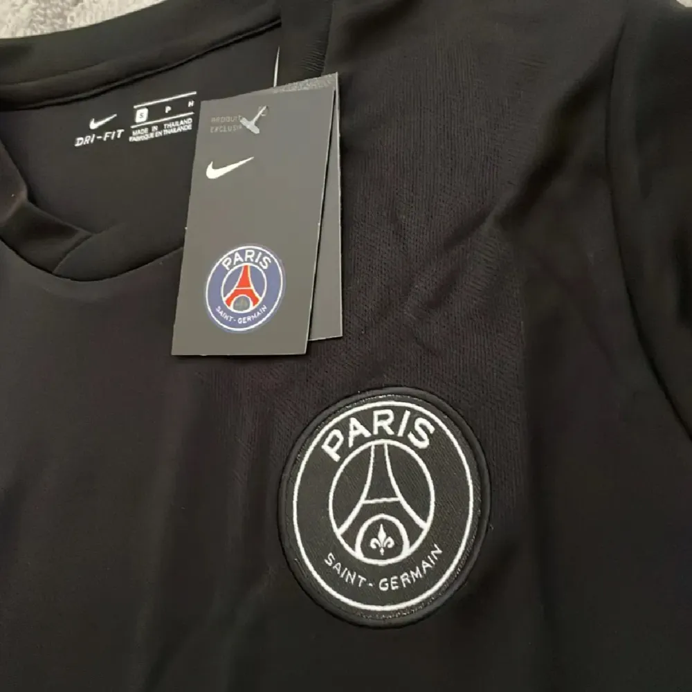 Säljer en snygg svart PSG x Balmain fotbollströja från Nike. Tröjan har en stilren design med PSG-loggan och Balmain Paris tryckt på framsidan. Den är kortärmad och tillverkad i ett bekvämt Dri-FIT material som håller dig sval. Perfekt för både träning och vardag!. T-shirts.