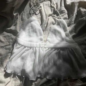 Vit ribbad halterneck topp - Säljer en superfin vit ribbad halterneck topp. Den är ärmlös och har en snygg knytning i nacken. Perfekt för sommardagar eller en festkväll. Toppen har en luftig och lätt känsla, öppen rygg. Toppen är oanvänd 