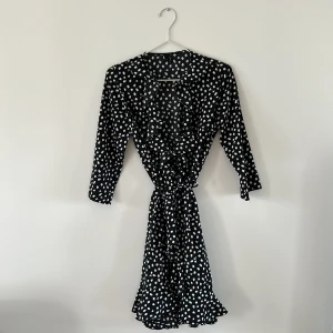 Klänning Vero Moda - Svartvit prickig klänning i omlottmodell, med volang och kortare ärmar. Storlek xs.