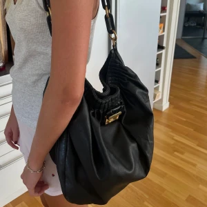 Marc Jacobs väska - Säljer min handväska från Marc Jacobs som jag ärvt av min mamma. Den är i 100% äkta skinn, perfekt skolväska eller vardagsväska. Den är rymlig med en liten innerficka, helt svart med gulddetaljer. Inuti är den röd med pussmunnar.