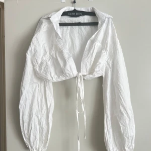 Vit croppad jacka från Galvin Green - Säljer en snygg vit croppad jacka från Galvin Green. Den har långa ärmar och en knytning framtill som ger en cool look. Perfekt för vår och sommar när du vill ha något lätt och stilrent.