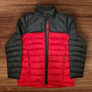 Röd och blå dunjacka från Polo Ralph Lauren - Säljer en snygg röd och blå dunjacka från Polo Ralph Lauren. Jackan har en dragkedja framtill och är perfekt för kyliga dagar. Den är i mycket bra skick och har långa ärmar. Passar perfekt för höst och vinter!