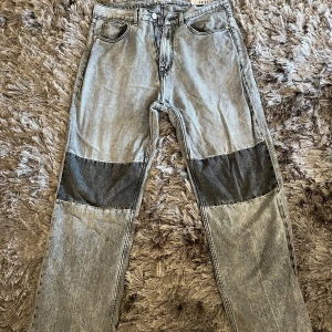 Grå jeans från Our Legacy - Säljer ett par grå jeans från Our Legacy i storlek 32. De har en cool patchwork-design med mörkare grå partier på knäna. Perfekta för en avslappnad stil och passar till både vardag och fest. Dragkedja och knapp framtill. Sköna och stilrena!