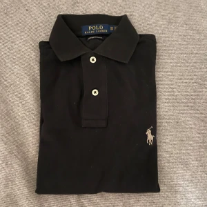 Svart Ralph Lauren Pike xs - Till salu: Svart Ralph Lauren Pike Tröja  Snygg och tidlös svart pike från Ralph Lauren. Perfekt för både vardagsbruk och mer formella tillfällen!  - Storlek: xs custom fit - Skick: Mycket bra skick  