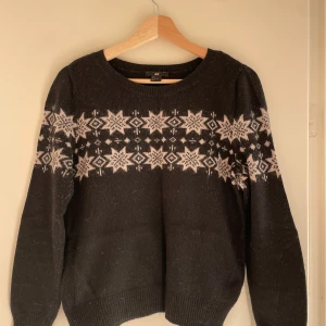 Svart tröja med mönster från H&M - Säljer en svart tröja från H&M i storlek S. Den har ett snyggt vitt mönster med stjärnor och snöflingor över bröstet. Perfekt för kyliga dagar med sin mysiga och varma känsla. Tröjan har långa ärmar och ribbade muddar vid ärmslut och nederkant.