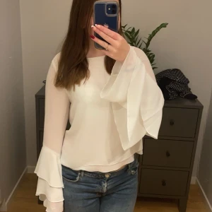 Vit blus med volangärmar från Bik Bok - Säljer en superfin vit blus från Bik Bok i storlek S. Den har långa ärmar med volangdetaljer och en liten öppning i ryggen.