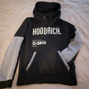 Svart och grå hoodie från Hoodrich - Säljer en snygg svart hoodie från Hoodrich med gråa ärmar och coola tryck både fram och bak. Perfekt för en avslappnad stil. Den har en stor ficka fram och en bekväm huva. Passar perfekt till höst och vår!