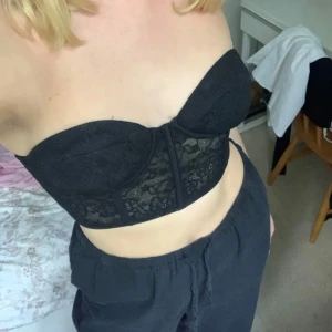 Svart spetsdetaljerad korsett - Säljer en snygg svart korsett med spetsdetaljer. Den är axelbandslös och har en tight passform som ger en fin siluett. Perfekt för festliga tillfällen eller när du vill känna dig extra fin. Använd ett fåtal gånger, så den är i mycket bra skick.