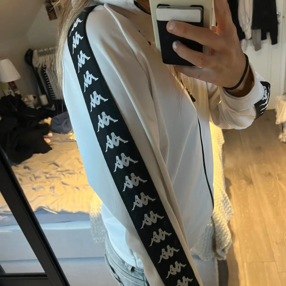 Säljer en snygg vit sweatshirt från Kappa med svarta detaljer och det klassiska Kappa-logotypbandet längs ärmarna. Jackan har dragkedja framtill och är perfekt för både träning och vardag. Den är i mycket bra skick och redo för nya äventyr! 🖤. Hoodies.