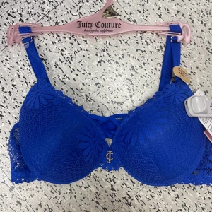 Blå spets-BH från Juicy Couture - Snygg blå BH från Juicy Couture i spets med ett elegant mönster. Den har justerbara axelband och en liten gulddetalj framtill. Perfekt för att känna sig både bekväm och stilren. Passar bra under alla typer av kläder och ger ett lyxigt intryck.