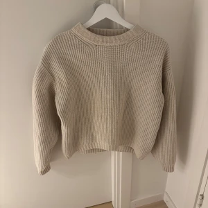 Beige stickad tröja - Säljer en supermysig beige stickad tröja i bra skick. Den har en kort passform och är perfekt för höst och vinter. Tröjan är långärmad och har en ribbad struktur.