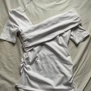 Vit offshoulder tröja från Zara - Säljer en superfin vit offshoulder tröja från Zara i storlek M. Tröjan har en snygg rynkdetalj på sidan och korta ärmar. Perfekt för sommarens alla fester eller en mysig dag på stan. Materialet känns mjukt och bekvämt. Passa på att fynda denna stilrena tröja!❣️