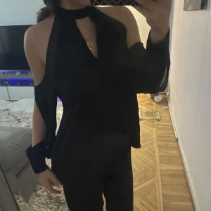 Svart halterneck topp - Snygg svart halterneck topp med öppen axeldesign. Perfekt för en utekväll eller fest. Toppen har en elegant passform och är tillverkad i ett mjukt material som ger en bekväm känsla. Den är stilren och lätt att matcha med olika outfits.