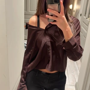 Brun/vinröd glansig satin skjorta  - Helt oanvänd ny kort klassisk brun skjorta/blus från Wera! Storlek dam 38 men passar som xs/s. Den har en lös passform och långa ärmar, materialet är jätteskönt, perfekt till fina tillfällen eller till vardags! Älskar verkligen tröjan, tog av prislappen då jag trodde att jag skulle hitta något tillfälle att ha den, men den har fortfarande inte kommit till användning. 