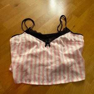 Rosa och vit randig linne från New Yorker - Säljer en söt rosa och vit randig linne från New Yorker. Den har svarta spetsdetaljer vid halsringningen och tunna axelband. Perfekt som nattlinne. Använd ett par gånger men i mycket bra skick! 