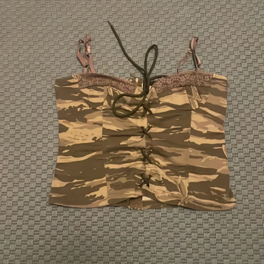 Säljer en cool camouflage korsett från Denny Rose i storlek L. Den har snörning framtill och justerbara axelband för perfekt passform. Perfekt för en edgy look!. Toppar.