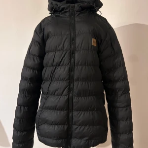 Svart pufferjacka från Urban Classics - Säljer en svart pufferjacka från Urban Classics i storlek S. Jackan är perfekt för kalla dagar med sin quiltade design och dragkedja framtill. Den har en praktisk huva och en innerficka med dragkedja för säker förvaring. Köpt från Zalando -basic bubble jacket. Perfekt vinterjacka, riktigt varm och go!