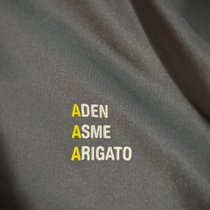 Svart hoodie från Axel Arigato - Säljer en snygg svart hoodie och byxor från Axel Arigato(ADENXASME)med dragkedja och gula detaljer. Perfekt för en avslappnad stil eller träning. Den har broderad text på bröstet och en bekväm passform. Passar både till vardags och sportiga aktiviteter.