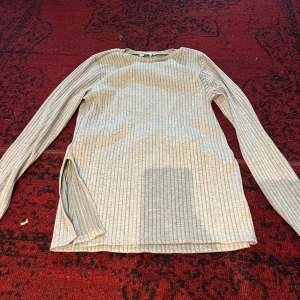 Grå ribbad långärmad tröja - Säljer en stilren grå ribbad tröja med långa ärmar. Perfekt för både vardag och lite kyligare dagar. Tröjan har en enkel design med en liten slits på sidan för extra stil. Passar bra till jeans eller kjol!