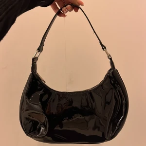 Väska! - En supersnygg lackerad svart axelarms väska från Gina tricot som rymmer jättebra och är i nyskick! Använd max 2 gånger. Köpt för 300.