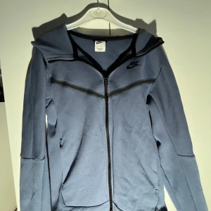 Blå Nike tech fleece - Säljer denna stilrena och populära Nike Tech Fleece-hoodie i färgen blågrå med svarta detaljer. Tröjan är i nyskick, använd ytterst få gånger och tvättad med omsorg. Inga fläckar, noppor eller slitningar 
