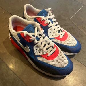 Nike Air Max i blå, vit och röd - Nike Air Max 90 – Ovanlig färgkombination, knappt använda  Säljer ett par Nike Air Max 90 i en ovanlig färgkombination av blått, vitt, rött och svart. Skorna är knappt använda och i mycket fint skick, nästan som nya.  Jag har inte hittat denna färgkombination till salu någonstans, så det verkar vara en sällsynt modell – perfekt för samlare eller någon som vill ha ett unikt par Air Max 90!  Storlek: 44,5
