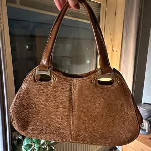 Snygg brun axelremsväska i skinn med stilrena detaljer och dragkedjor. Väskan är köpt second hand, märke: Scala. Rymlig väska där allt man behöver får plats🤗hör av dig vid frågor eller fler bilder.