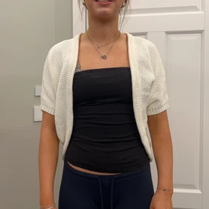 Vit stickad bolerotopp - Säljer en söt vit stickad bolerotopp med korta ärmar. Perfekt för att lägga till en extra touch till din outfit. Passar bra över en klänning eller topp.