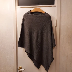 Grå poncho  - Säljer en stilren grå poncho i mjukt syntetmaterial från  Cubus. Perfekt för att hålla sig varm under kyliga dagar. Ponchon har en enkel design utan ärmar och är lätt att matcha med olika outfits. Använd fåtal gånger. 