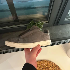 Grå sneakers från Axel Arigato - Snygga grå sneakers från Axel Arigato i mocka med en stilren design. Skorna är i jätte bra skick och dom har inga defekter. Hör av er för frågor och funderingar! Priset kan diskuteras