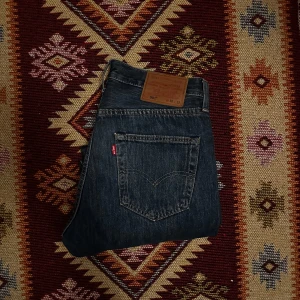 Levis 501 jeans - Klassiska Levis 501 jeans i mörkblå denim i gott skick. De har en rak passform och knappgylf. Perfekta för en avslappnad stil med fem fickor och den ikoniska Levis-lappen baktill. Priset går ner vid snabb affär! Obs byxorna har sytts till en längd närmare 30.